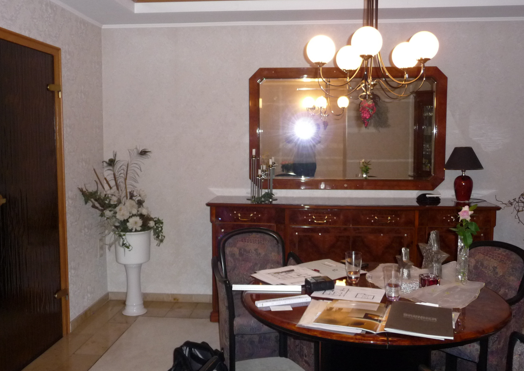Klassisches Esszimmer mit Holz-Kommode, großem Wandspiegel, Kronleuchter und Blumendeko