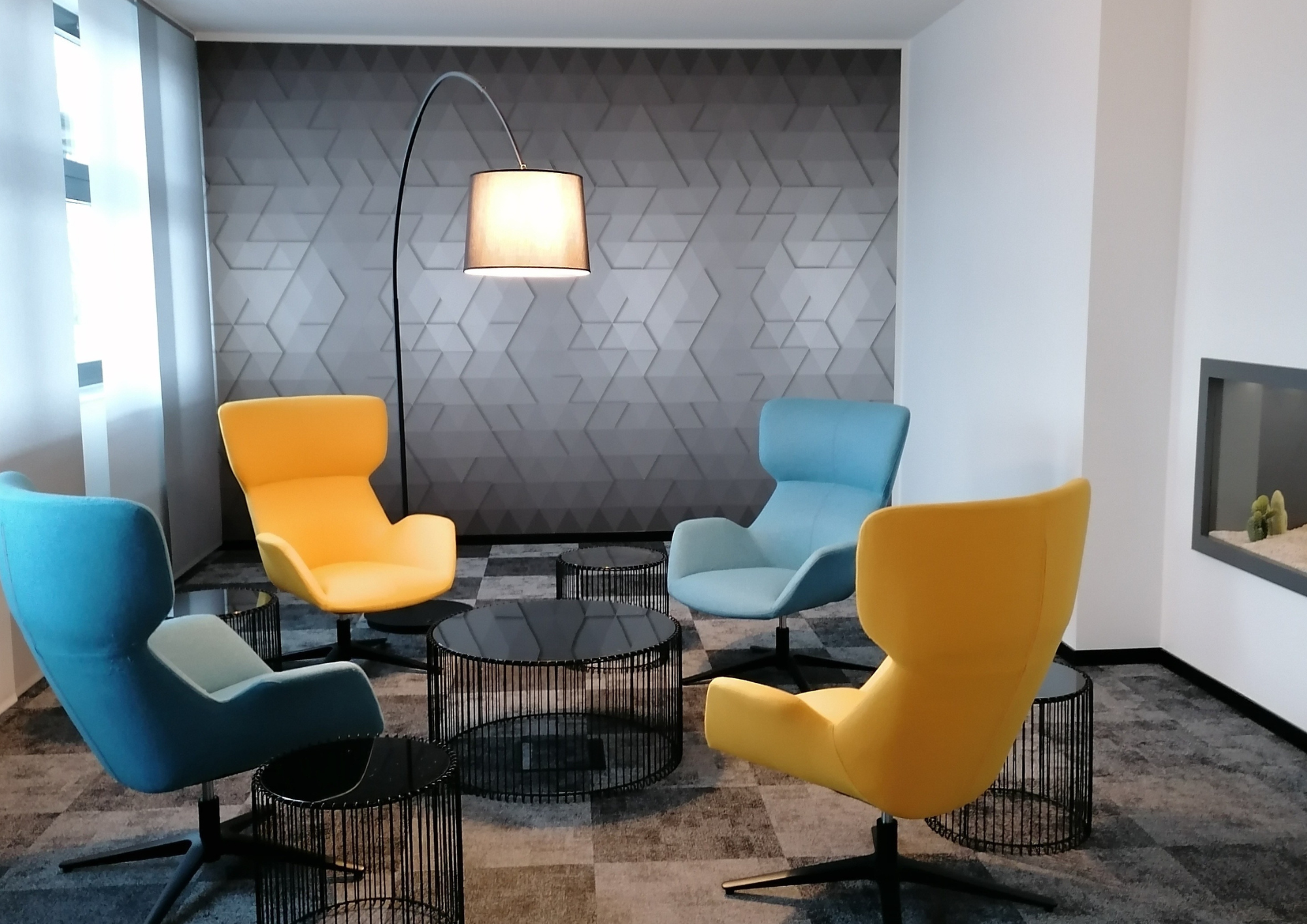 Modern eingerichtete Lounge mit gelben und blauen Sesseln, Designerlampe und geometrischer Wandgestaltung
