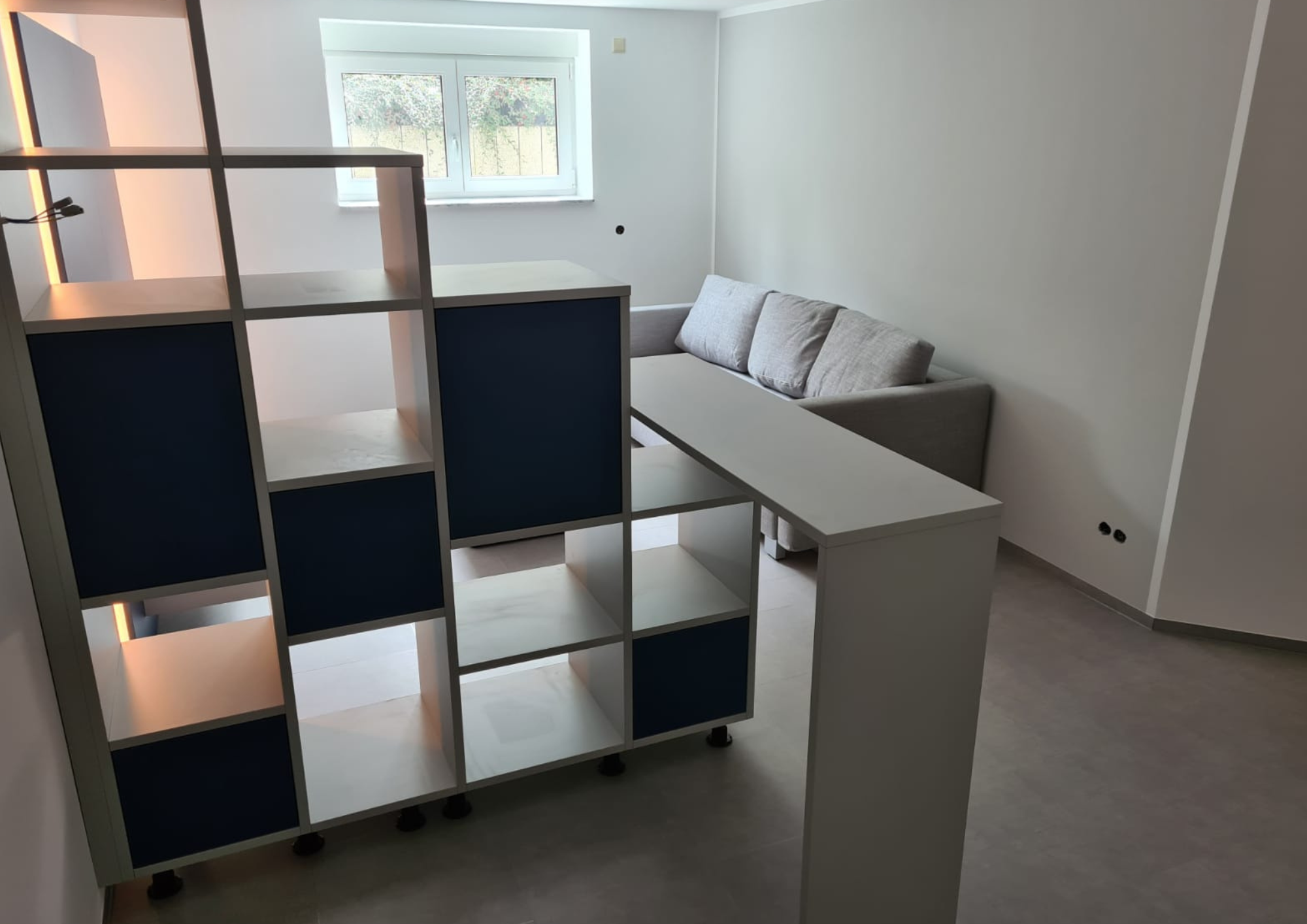 Blick durch den Raumteiler auf ein graues Sofa vor hellem Fenster