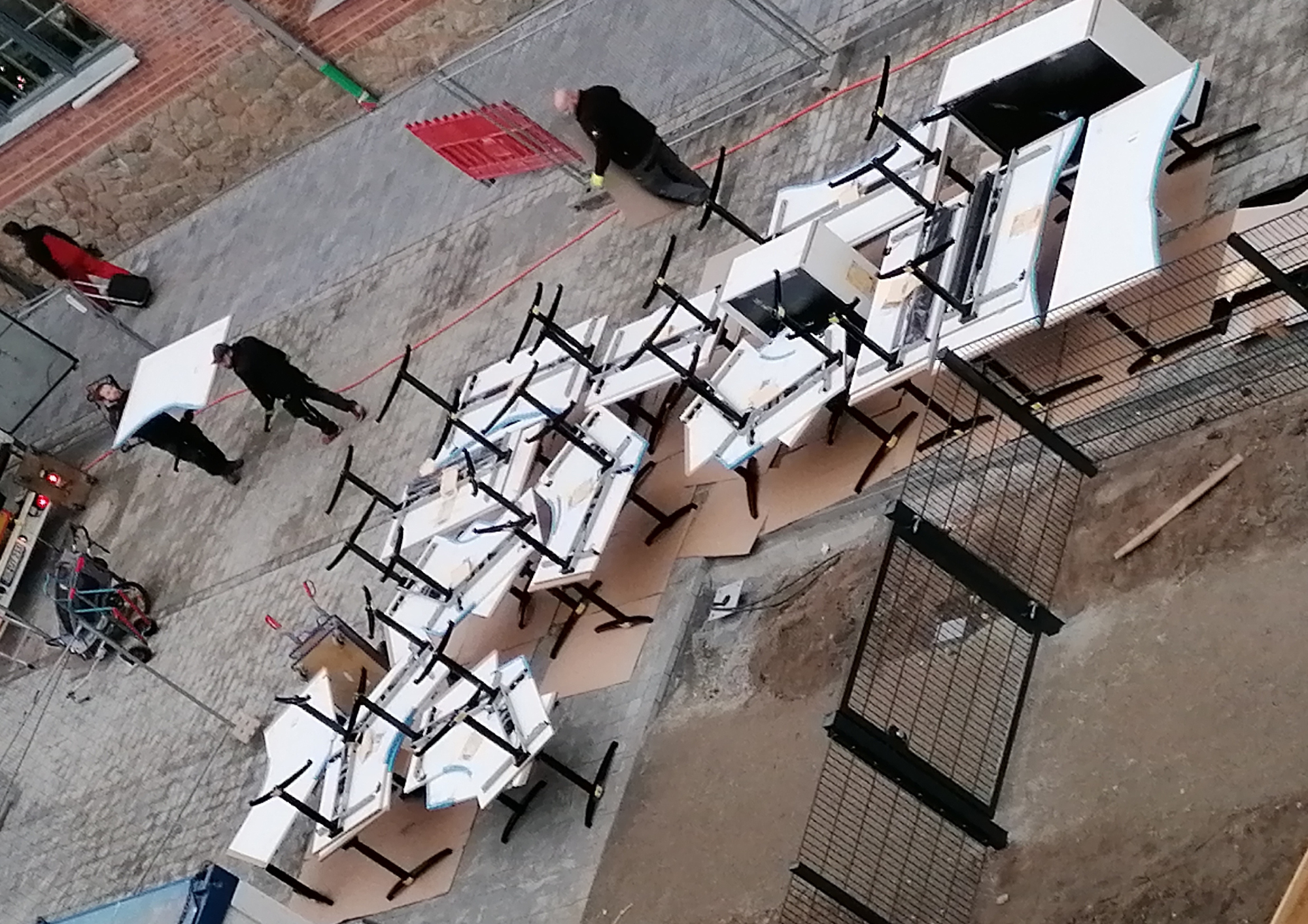 Zahlreiche Tische mit Metallgestellen stehen gestapelt auf dem Hof vor einem Bürogebäude