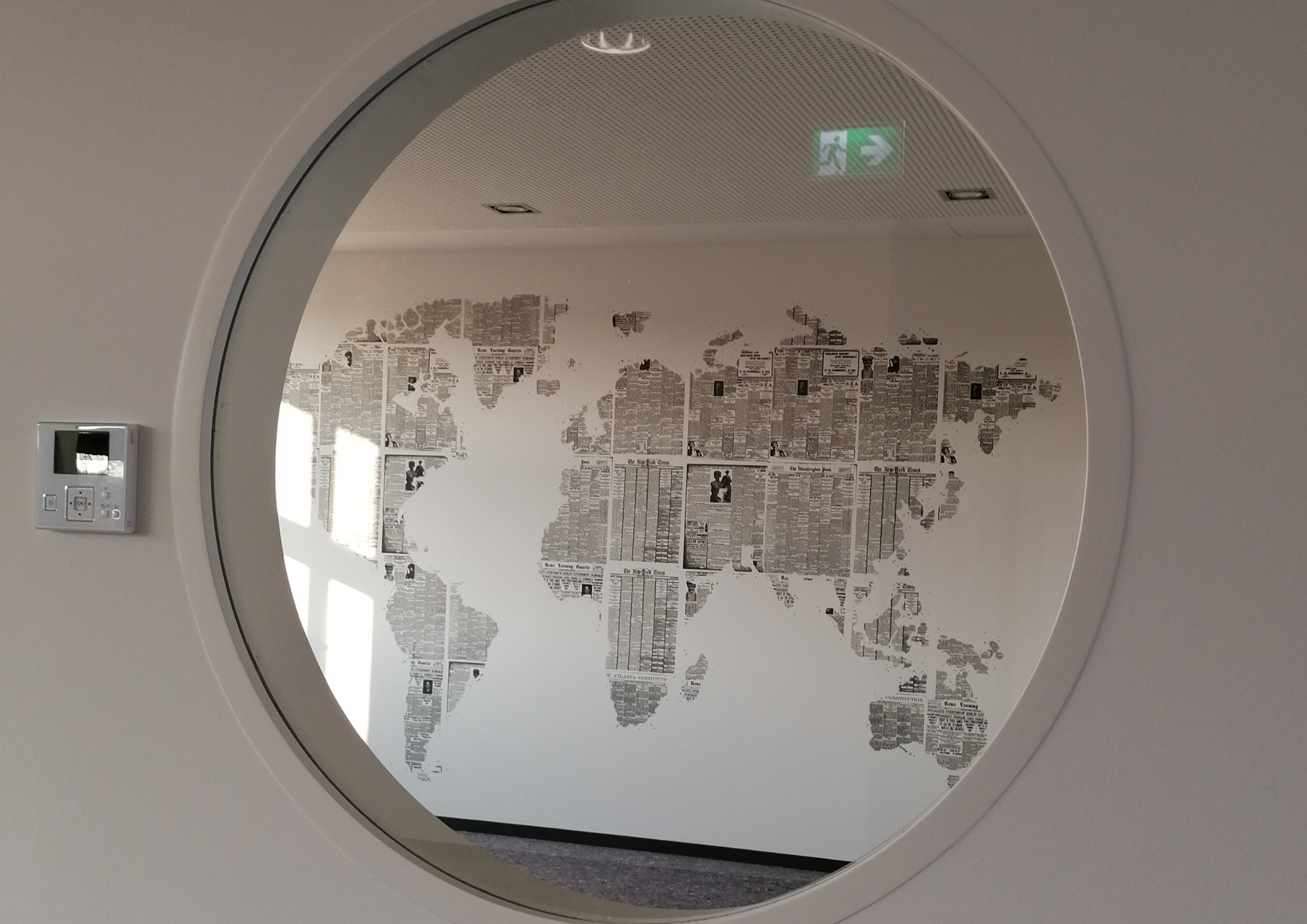 Wand mit Weltkarte aus Zeitungsausschnitten, durch ein rundes Fenster fotografiert