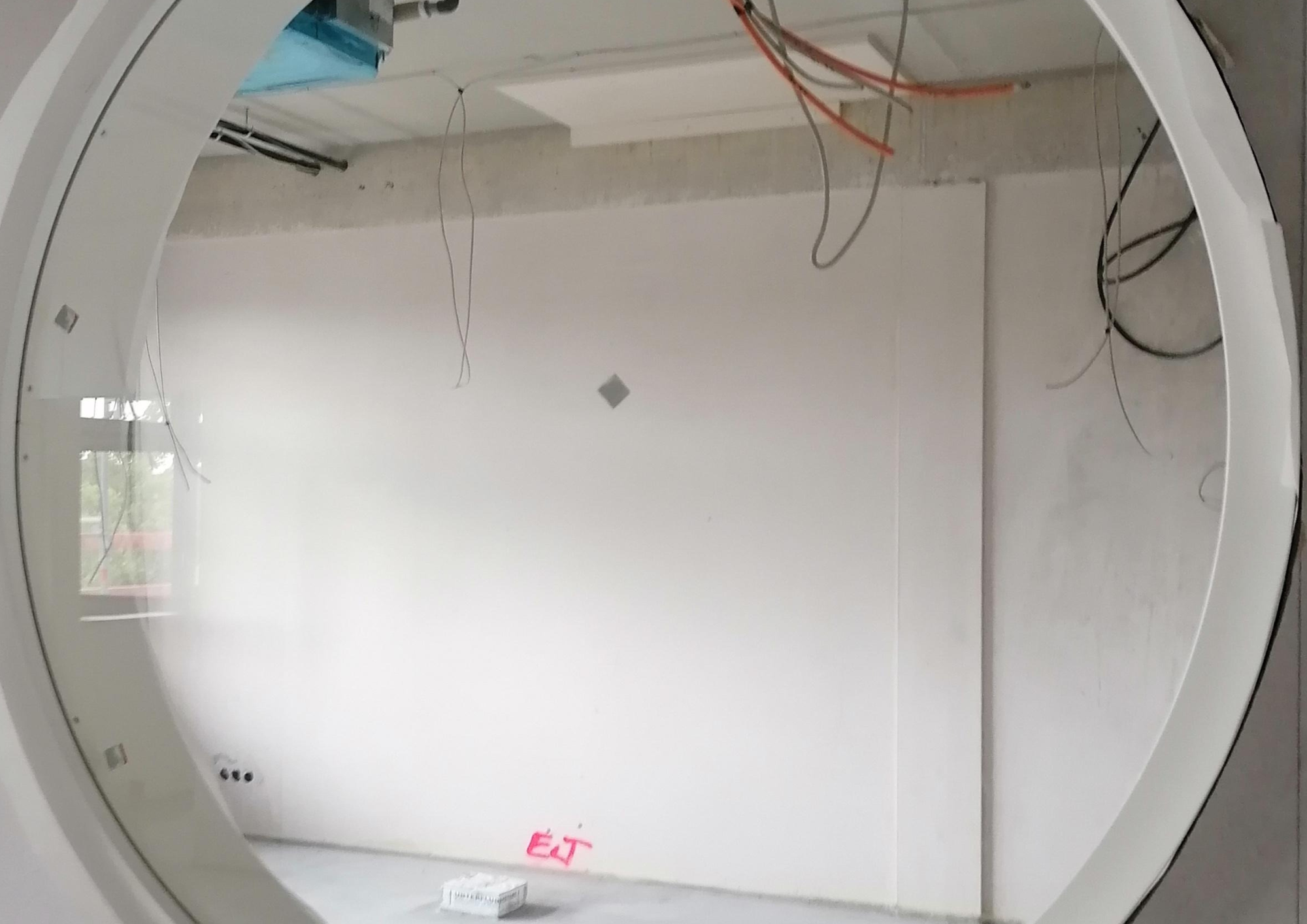 Unfertiger Büroraum mit runder Glasöffnung in der Wand und sichtbarer Verkabelung
