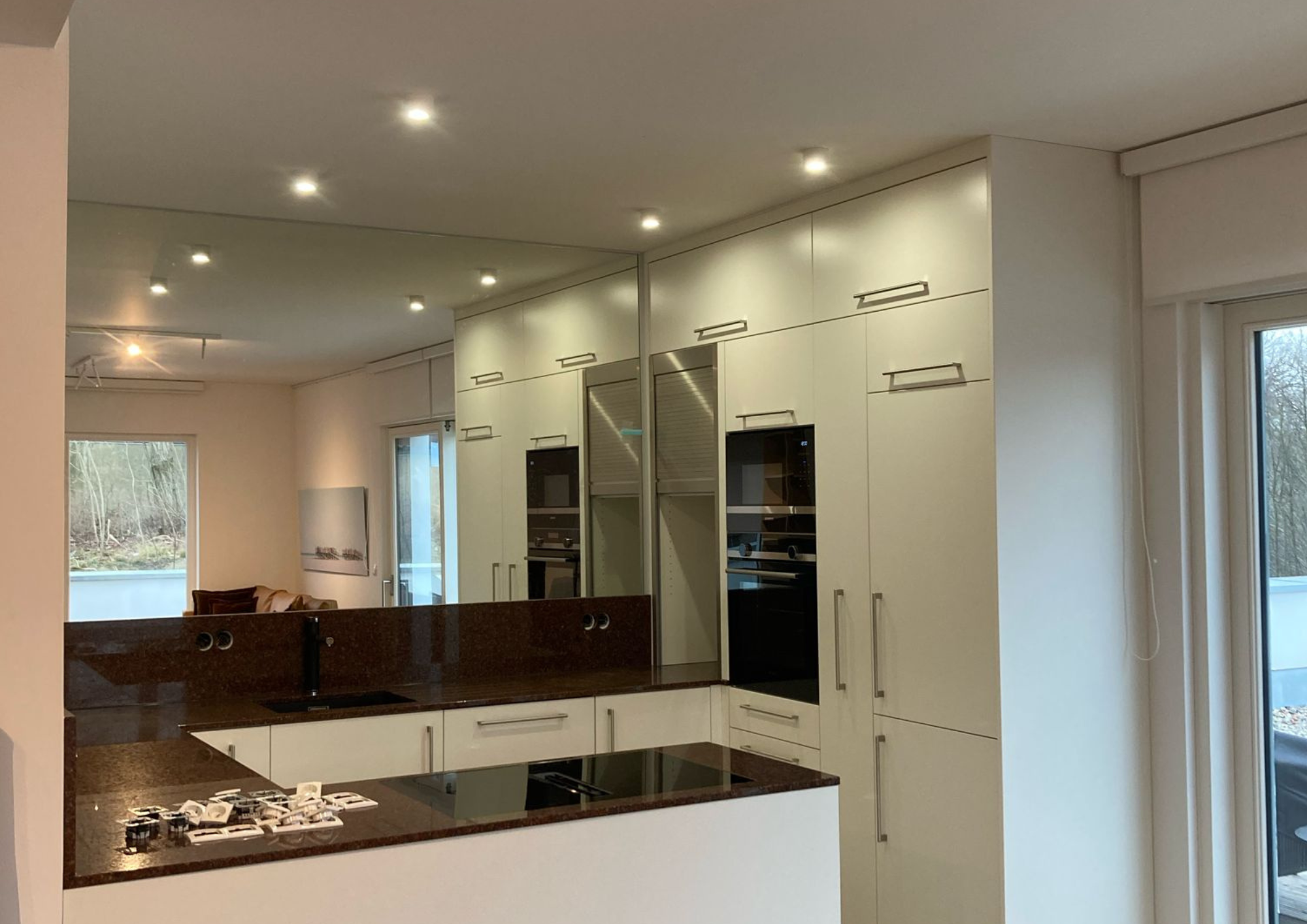 Moderne Einbauküche mit weißen Fronten, Spiegelflächen und dunkler Arbeitsplatte in einer Ferienwohnung auf Rügen