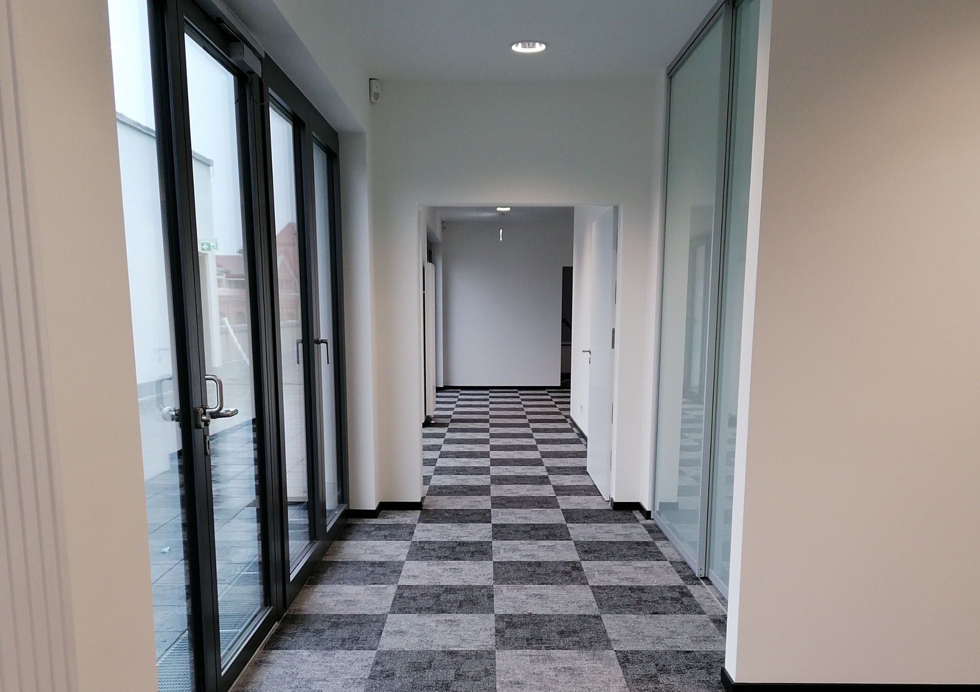 Neuer Büroflur mit grauen Teppichfliesen und großen Glasfronten zur Terrasse
