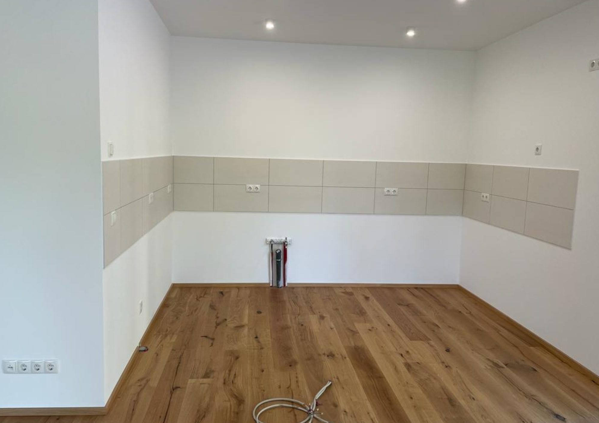 Leerer Küchenraum mit vorbereiteten Anschlüssen und Fliesenspiegel vor dem Einbau in einer Ferienwohnung auf Rügen