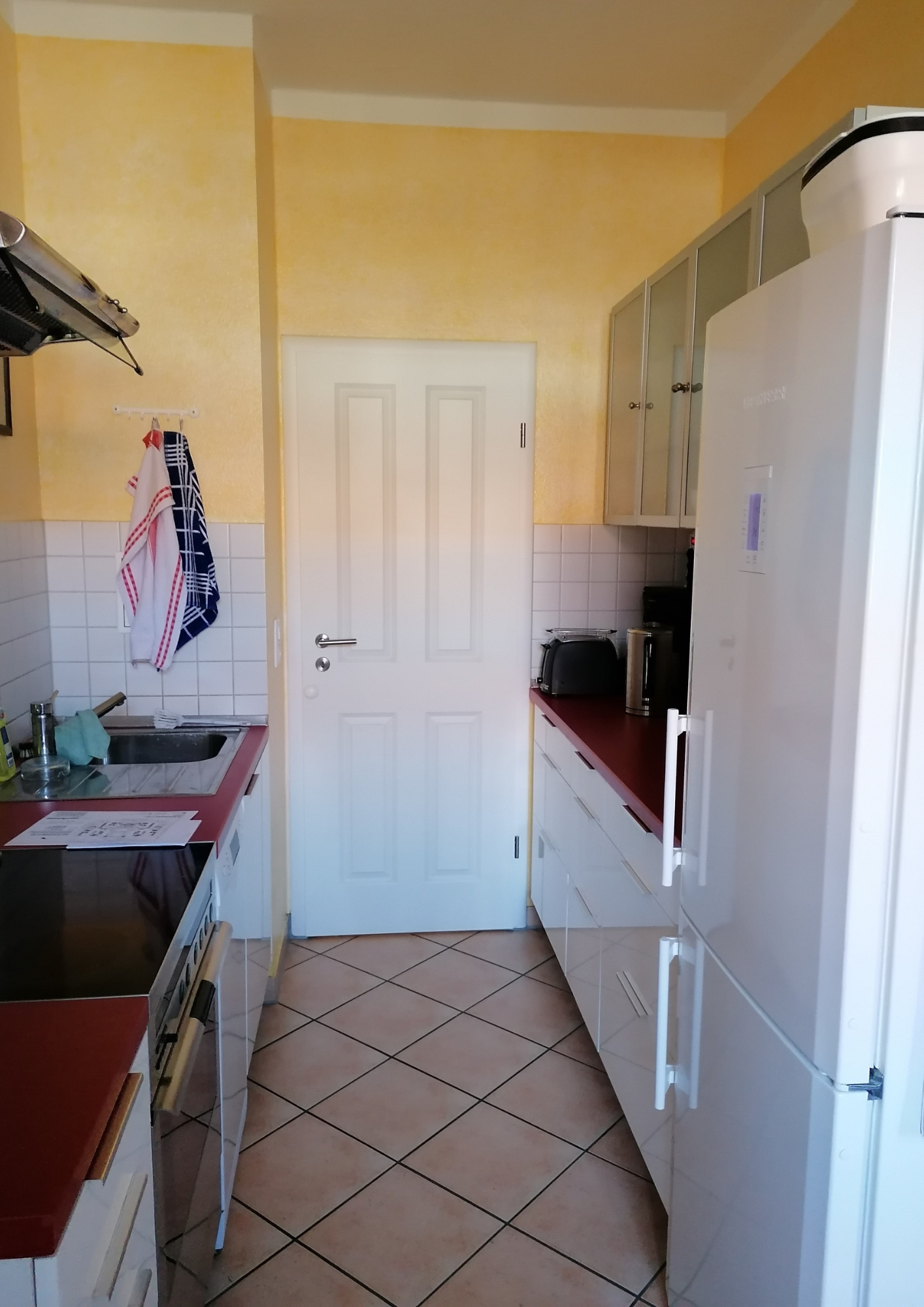 Alte Küche vor der Renovierung mit Fliesenboden und gelben Wänden.