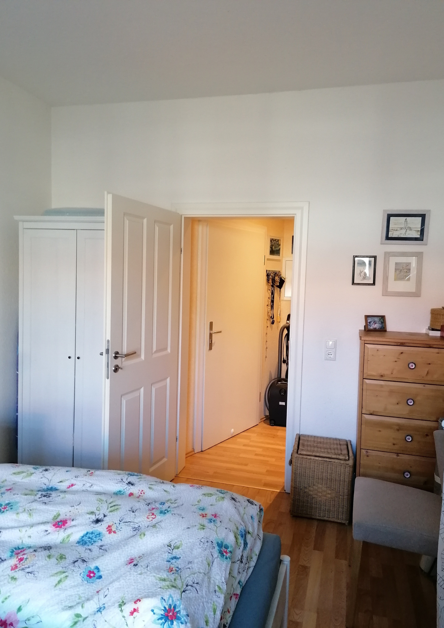 Schlafzimmer mit Holzkommode und Blick in den renovierten Flur.