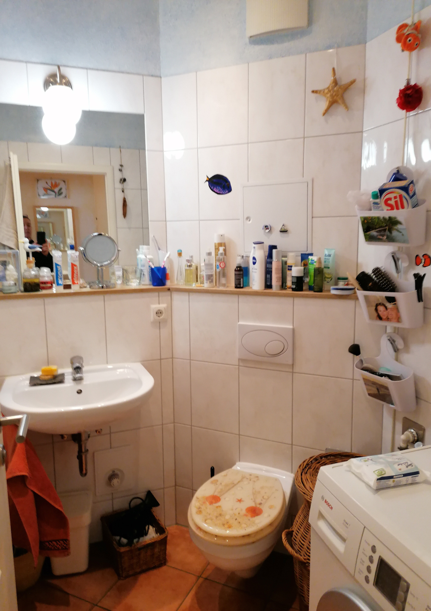 Altes Badezimmer mit Waschbecken, Toilette und zahlreichen Ablagen vor dem Umbau.