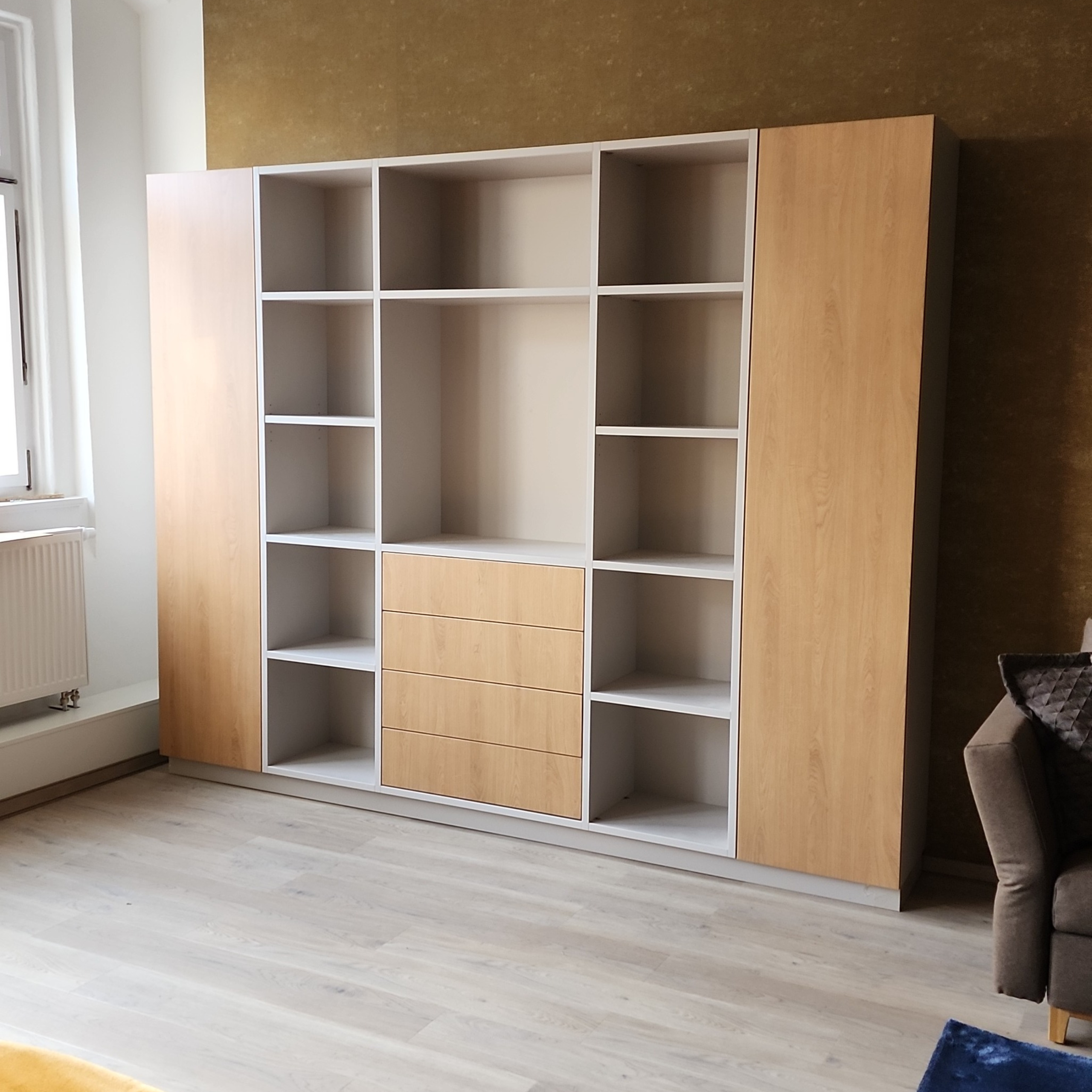 Regalwand mit offenen Fächern und Holzoptik im renovierten Altbau in Leipzig, kombiniert mit goldener Wand und Stuckdecke – modernes Möbeldesign trifft Altbaucharme.